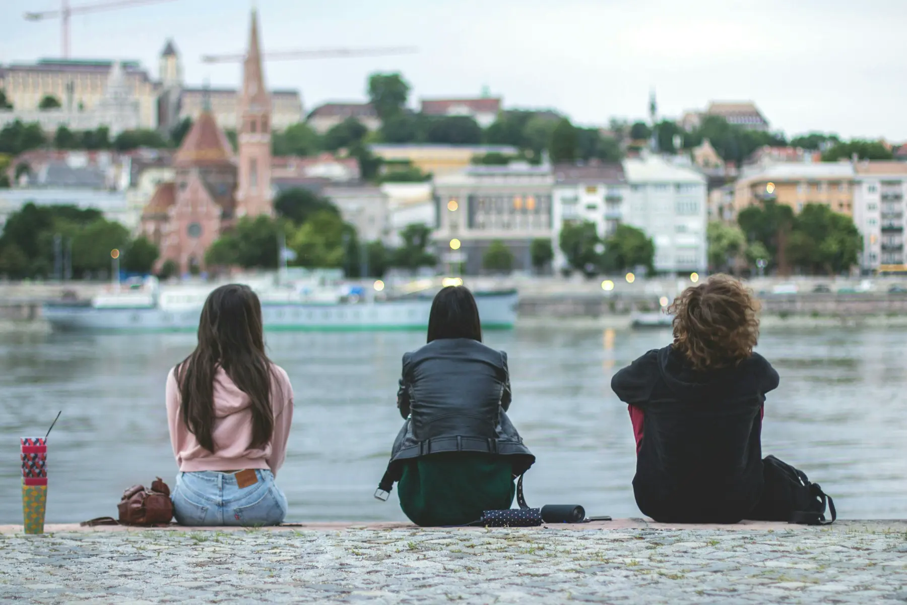 Tre ragazzi seduti sul lungofiume guardano la città dall'altra riva
