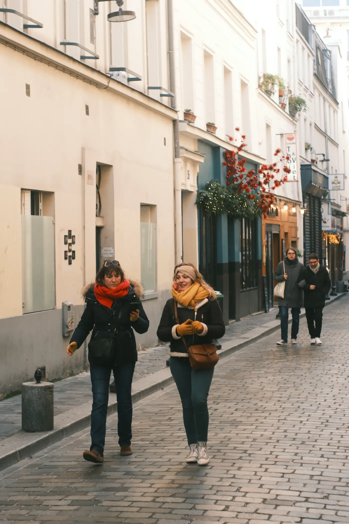 Due ragazze con sciarpe gialle e arancioni camminano in una via acciottolata di Parigi